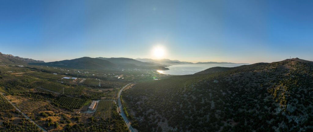 Εναέρια θέα ηλιοβασιλέματος πάνω από το Elaiodentron eco House με θέα το λόφο με κέδρους, το χωριό Παχεία Άμμος και τη θάλασσα στην Ανατολική Κρήτη
