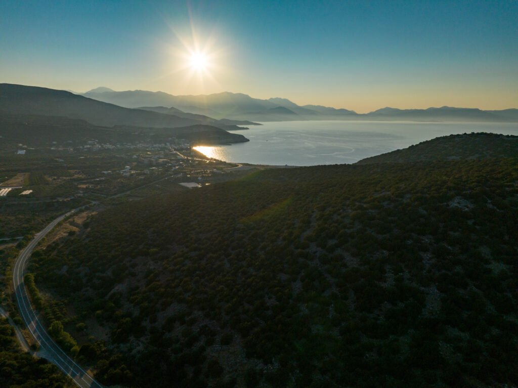 Ηλιοβασίλεμα από drone πάνω από το Elaiodentron eco House με θέα το λόφο με κέδρους, το χωριό Παχεία Άμμος και τη θάλασσα στην Ανατολική Κρήτη